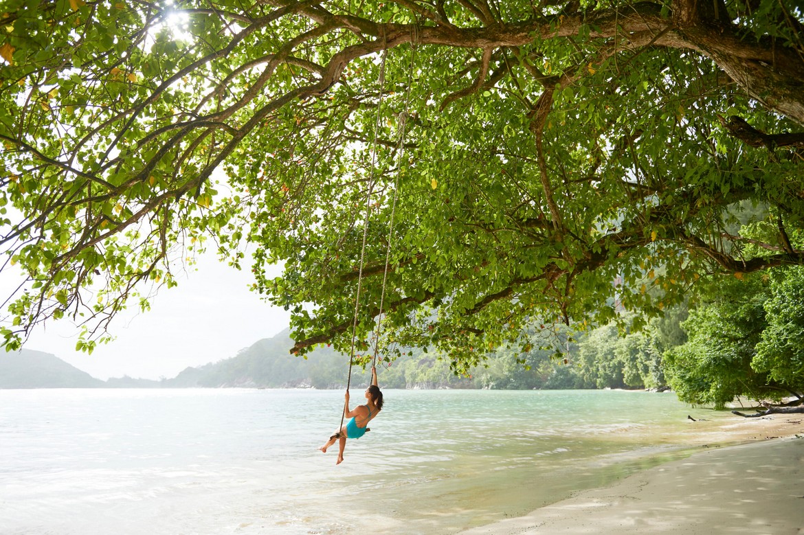 CONSTANCE EPHELIA SEYCHELLES Lady swinging on tree swing over beach