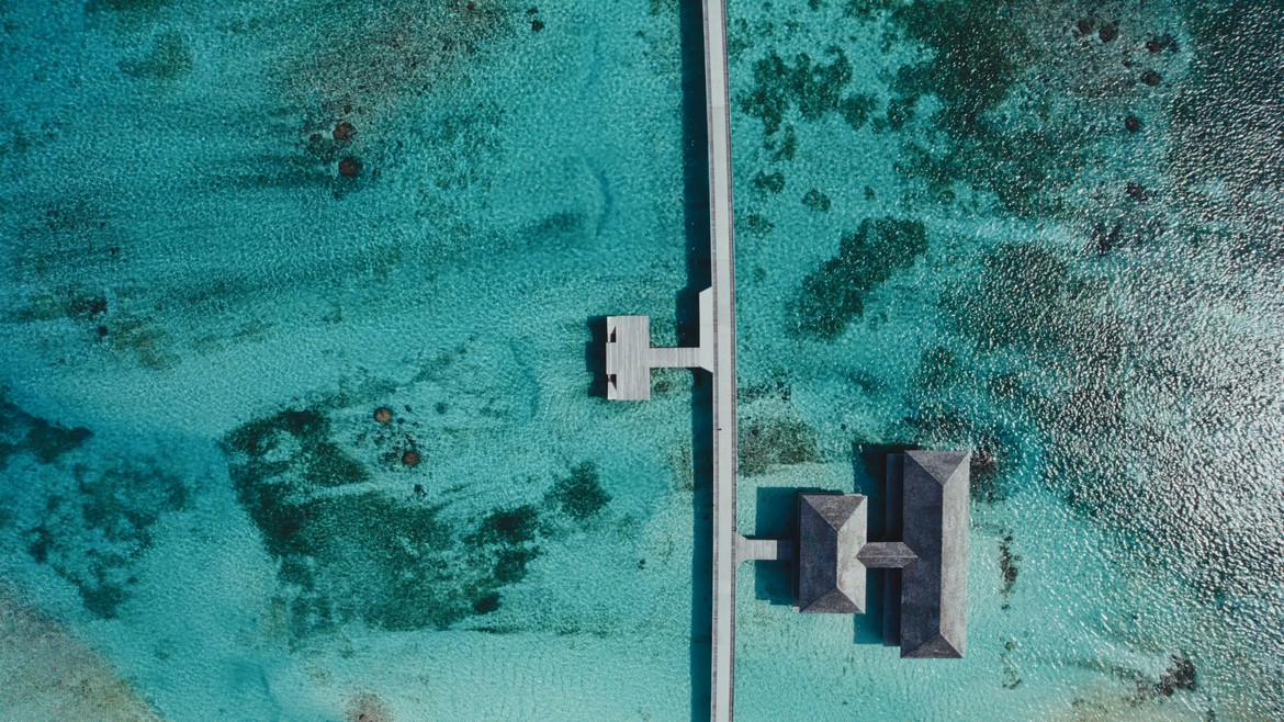 Aerial view of Jawakara Dheru Island villas surrounded by turquoise waters and coral reefs
