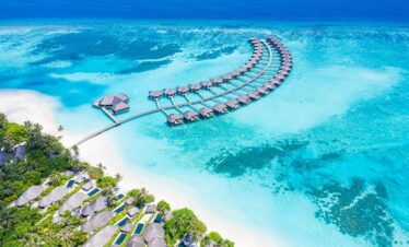 Aerial view of Sun Siyam Iru Fushi featuring a crescent of overwater villas surrounded by vibrant turquoise waters