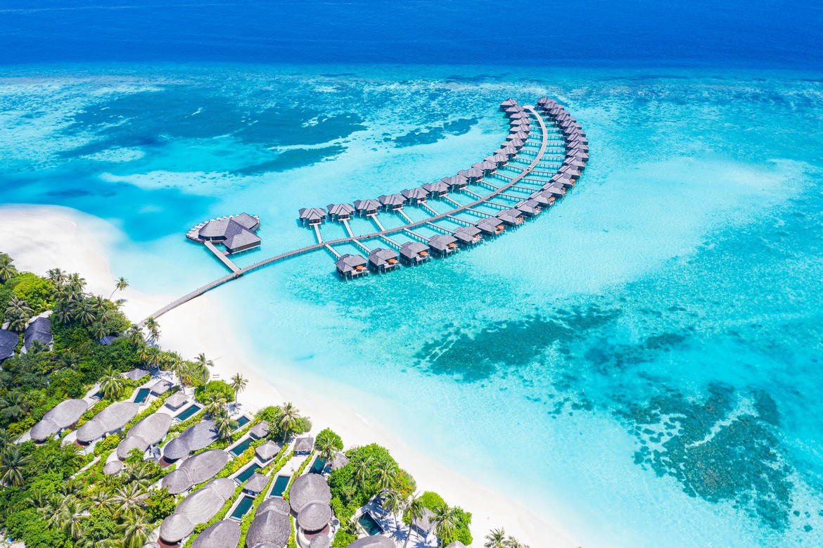 Aerial view of Sun Siyam Iru Fushi featuring a crescent of overwater villas surrounded by vibrant turquoise waters