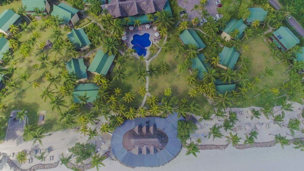 Aerial view of lush tropical landscape with green roofs and a pool at Paradise Sun