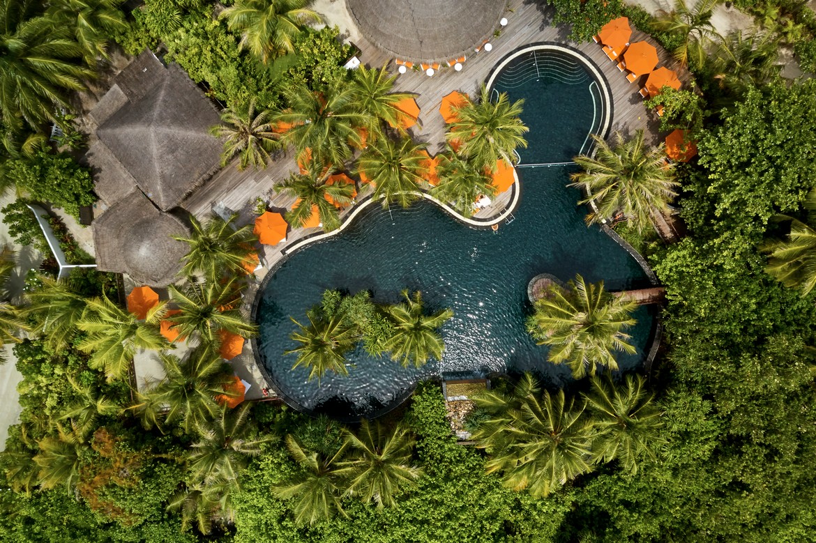 Aerial view of the Sun Siyam Iru Fushi pool area surrounded by dense tropical vegetation and vibrant palm trees