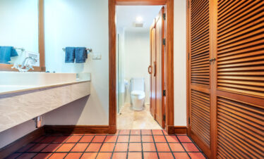 Bathroom at Chada Thai Village featuring a sink, wooden doors, and tiled flooring leading to a toilet area