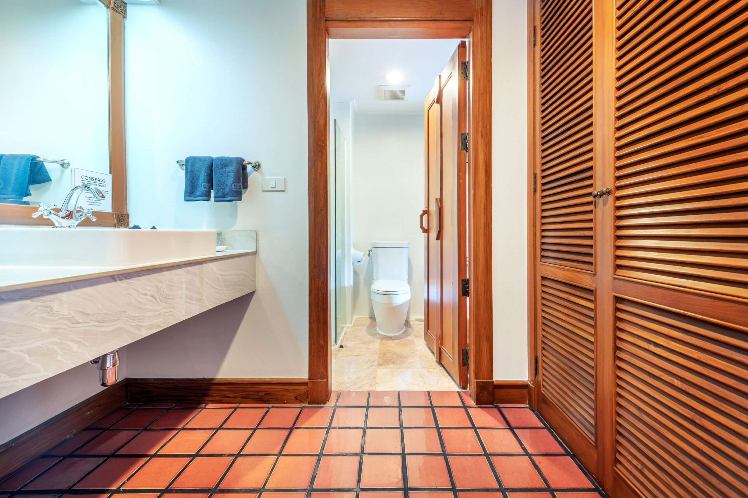Bathroom at Chada Thai Village featuring a sink, wooden doors, and tiled flooring leading to a toilet area