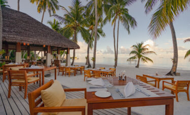 Beachfront dining area at Ayada Maldives under palm trees overlooking the calm sea