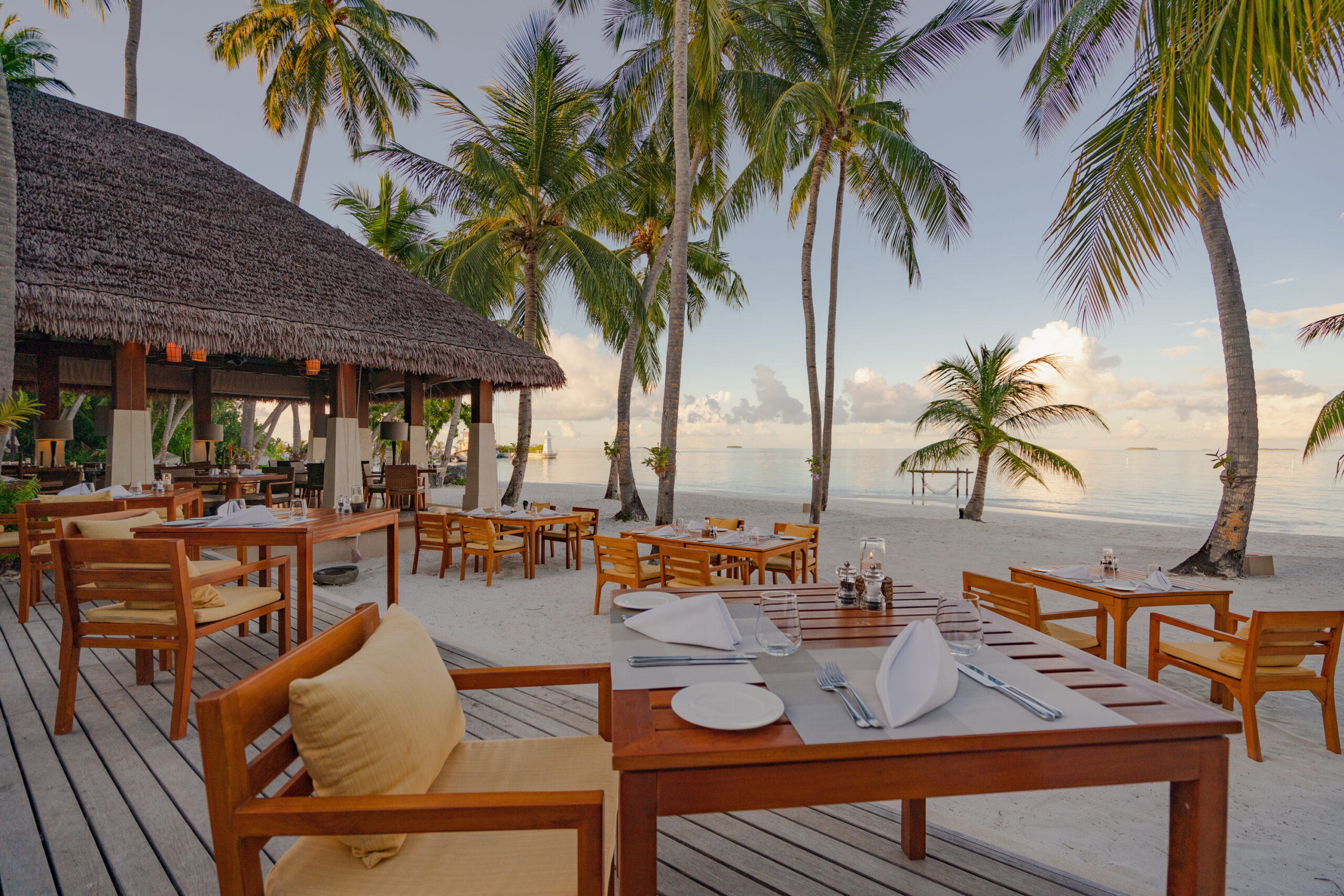 Beachfront dining area at Ayada Maldives under palm trees overlooking the calm sea