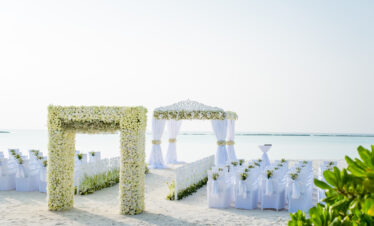 Beachfront wedding setup at Sun Siyam Iru Fushi with a floral arch and white chairs facing the serene ocean