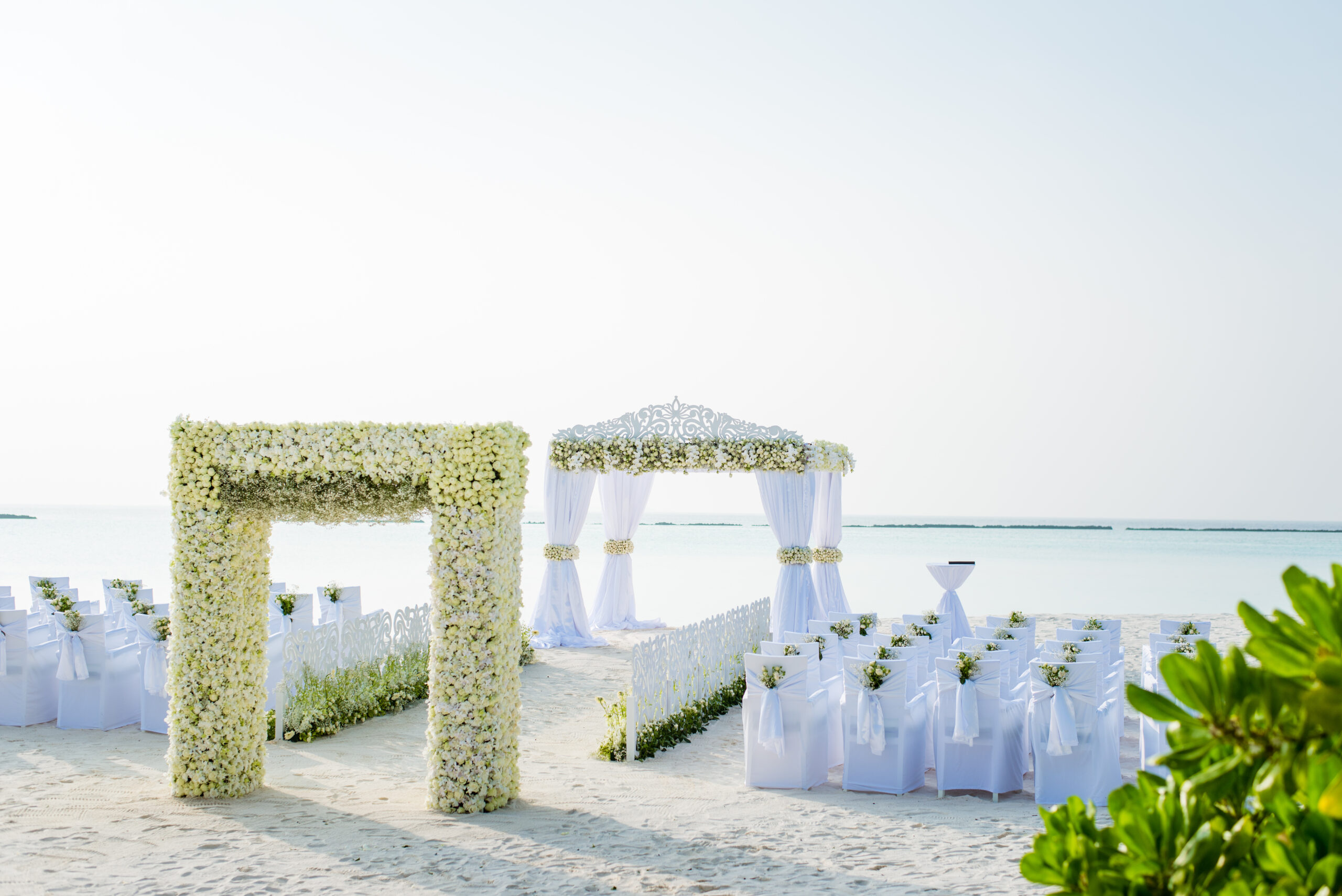 Beachfront wedding setup at Sun Siyam Iru Fushi with a floral arch and white chairs facing the serene ocean