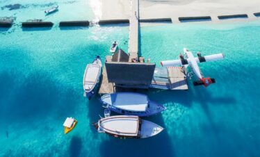 Boats and a seaplane docked at a pier in Constance Moofushi with clear blue water and white sand beach