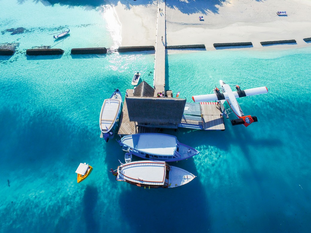 Boats and a seaplane docked at a pier in Constance Moofushi with clear blue water and white sand beach