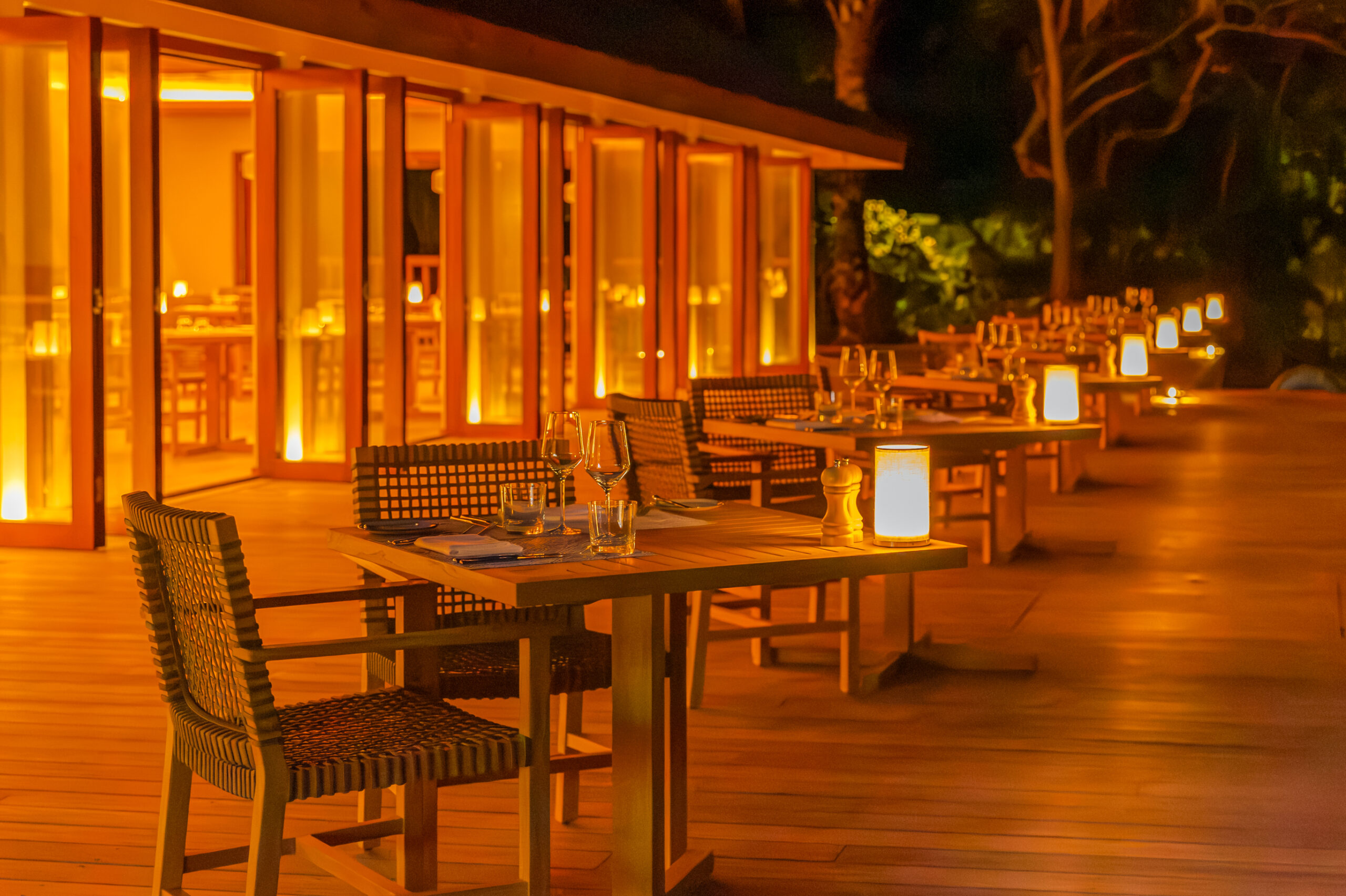 Candlelit outdoor dining area at Meeru Island Resort with warm amber lighting creating a cozy atmosphere at night