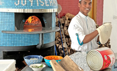 Chef preparing pizza in a wood fired oven at Joy Island