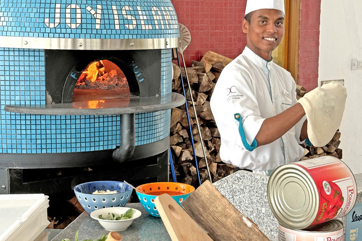 Chef preparing pizza in a wood fired oven at Joy Island