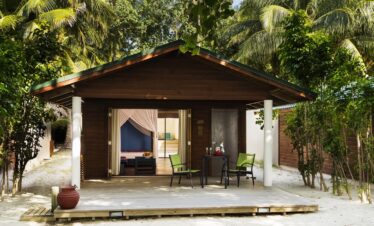 Cozy beach villa at Meeru Island Resort with a private terrace surrounded by tropical greenery and a sandy path