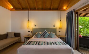 Cozy bed in a Vilamendhoo villa with soft lighting and a tropical garden view