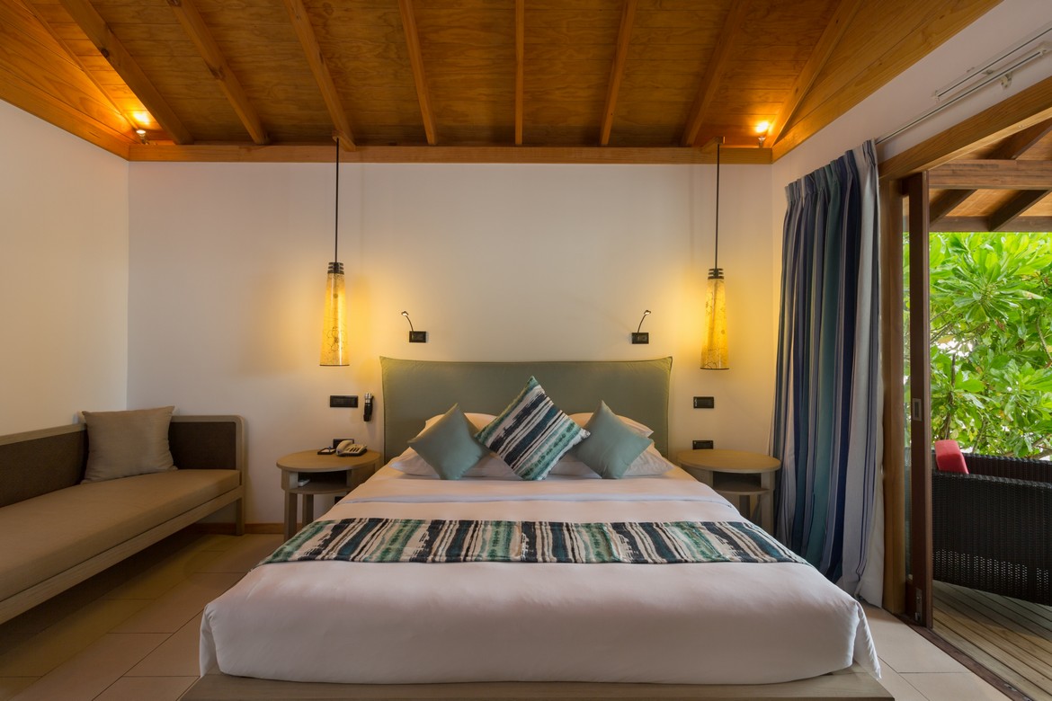 Cozy bed in a Vilamendhoo villa with soft lighting and a tropical garden view