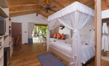 Cozy suite at Meeru Island Resort with a canopy bed and direct access to a private patio with sun loungers