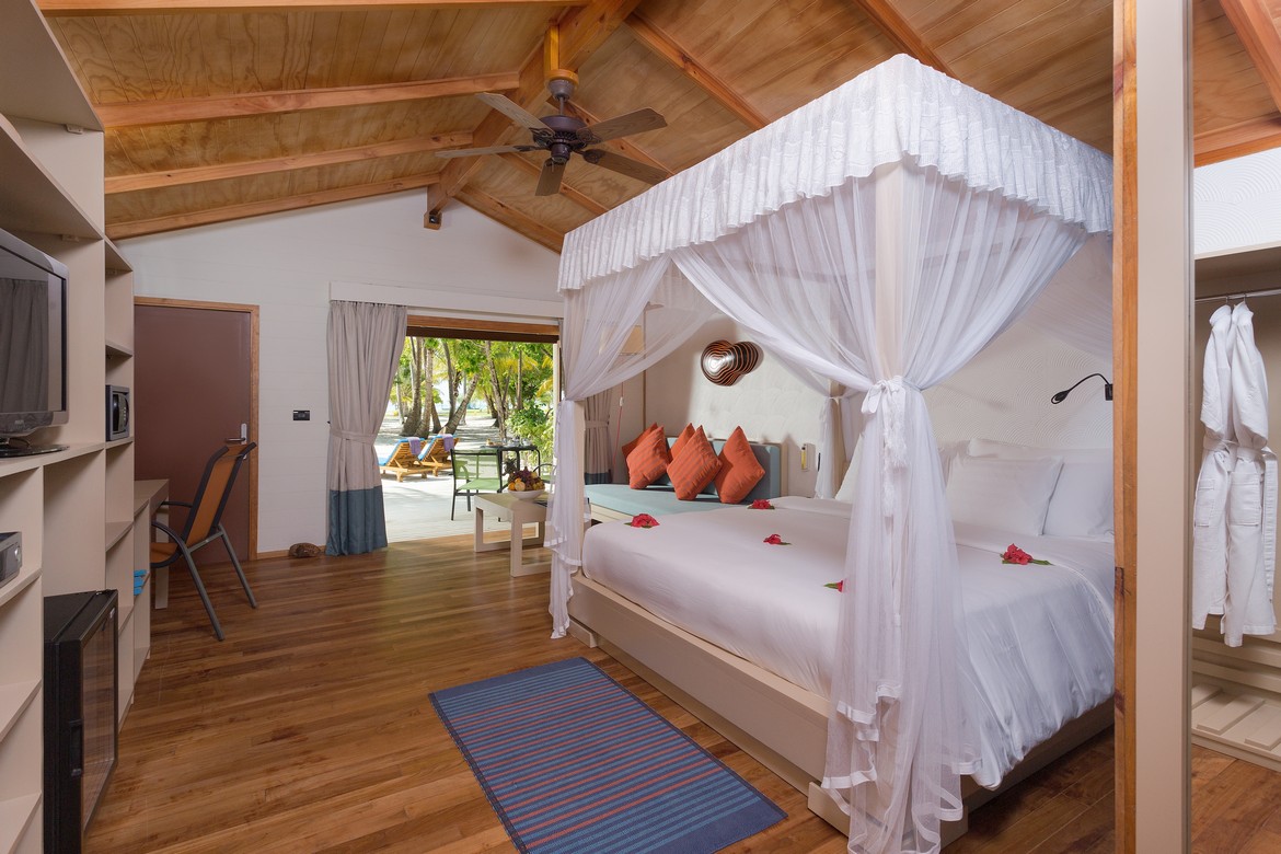Cozy suite at Meeru Island Resort with a canopy bed and direct access to a private patio with sun loungers
