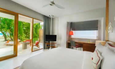 Dhigali resort bedroom with large windows overlooking tropical greenery
