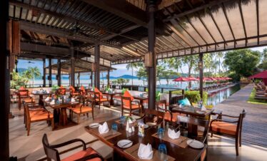 Dining area with ocean view at The Vijitt Resort featuring wooden tables and vibrant cushions