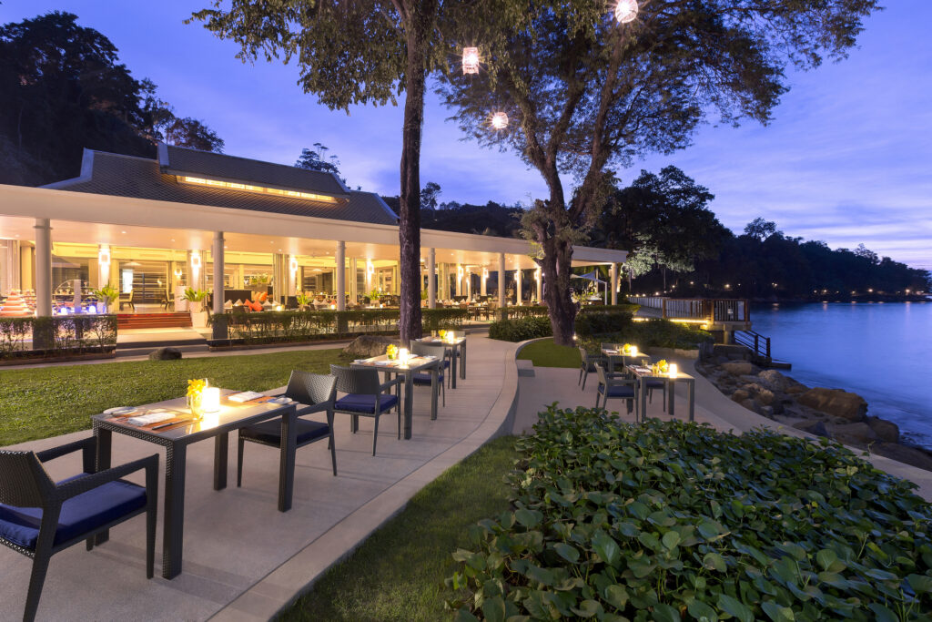 Evening dining setup by the water at Amari Phuket with glowing lights and greenery