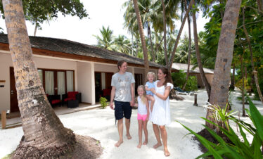 Family enjoying a walk near beachside villas at Vilamendhoo surrounded by palm trees and lush greenery