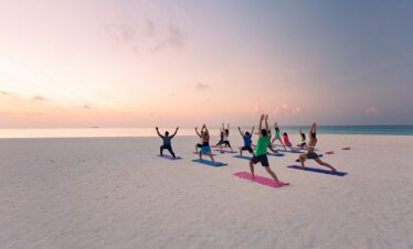 Group yoga session on the beach at Meeru Island Resort during sunrise with the ocean in the background