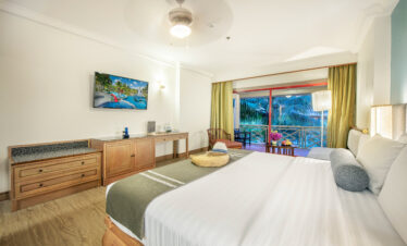 Guest room at Chada Thai Village with a large bed, balcony view, and wooden furniture throughout