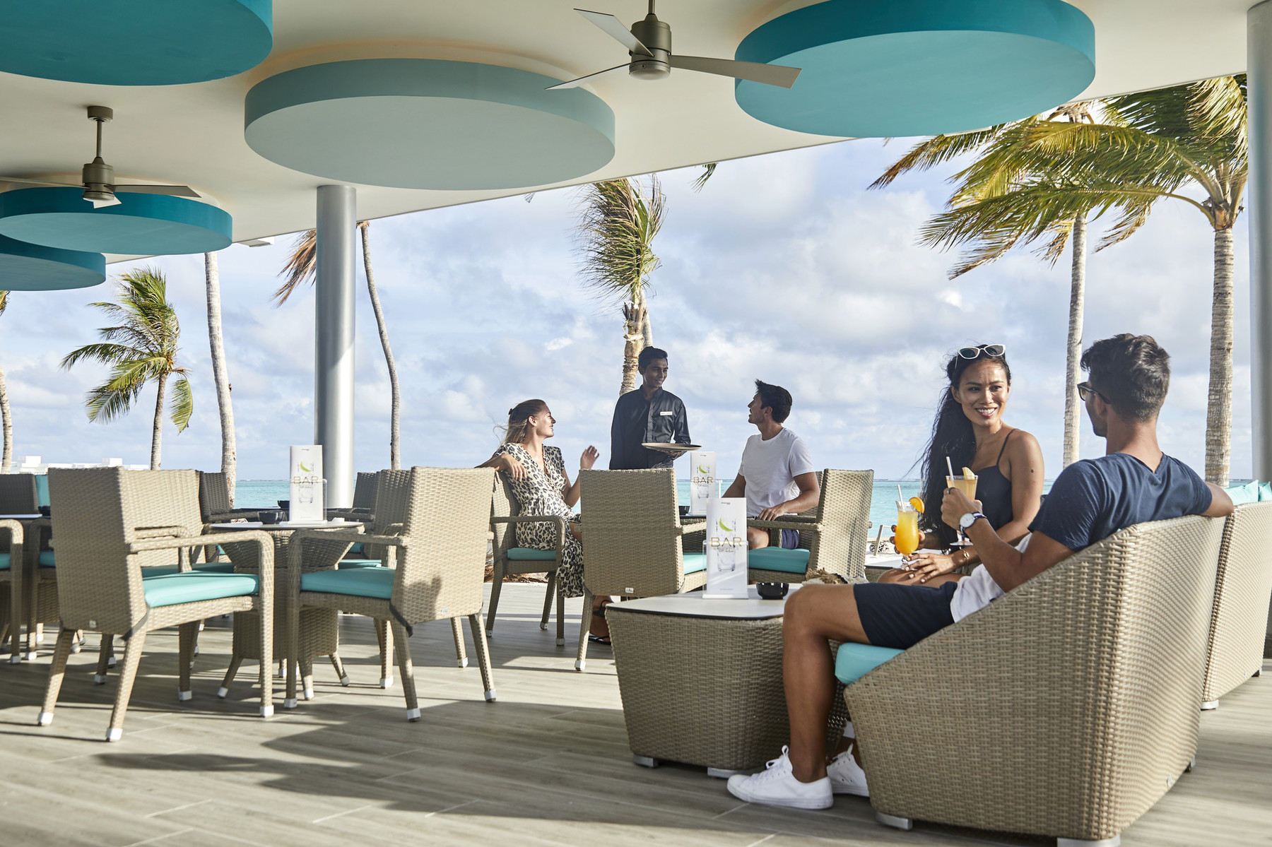 Guests enjoying drinks at an outdoor seating area at Riu Atoll with ocean views