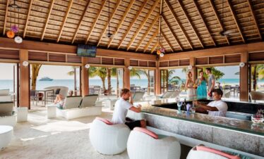 Guests relaxing at a beachfront bar with a thatched roof at Meeru Island Resort with ocean views and refreshing drinks