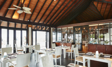 Interior of a Sun Siyam Iru Fushi restaurant featuring wooden ceilings and large glass windows with ocean views