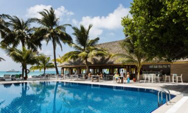 Inviting pool area at Meeru Island Resort surrounded by palm trees with a view of the ocean and a beachfront bar