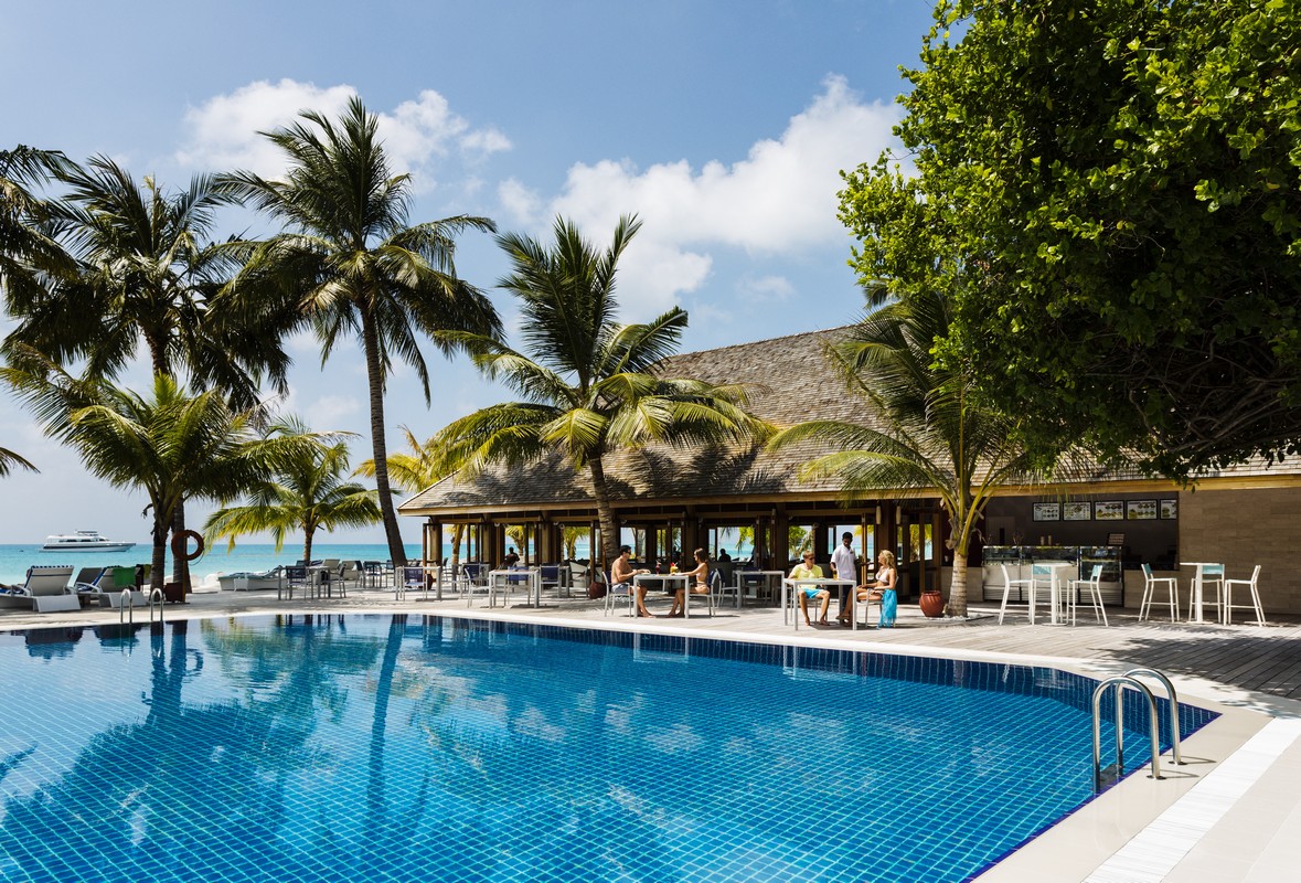 Inviting pool area at Meeru Island Resort surrounded by palm trees with a view of the ocean and a beachfront bar