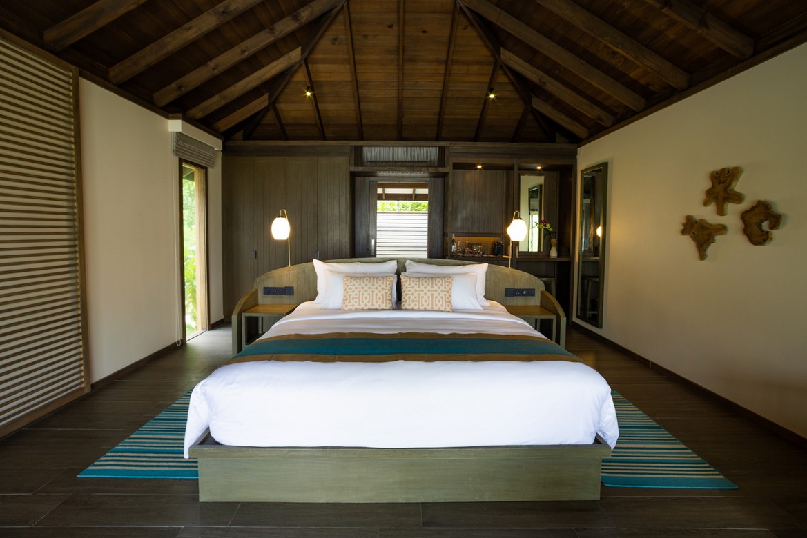 Jawakara Dheru Island beach villa interior with a luxurious bed under a vaulted wooden ceiling