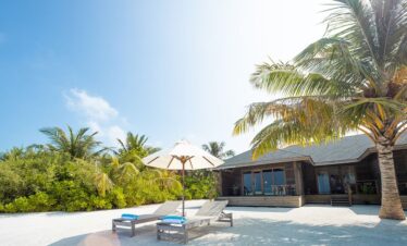 Jawakara Dheru Island beachfront villa with sun loungers under palm trees on white sandy beach
