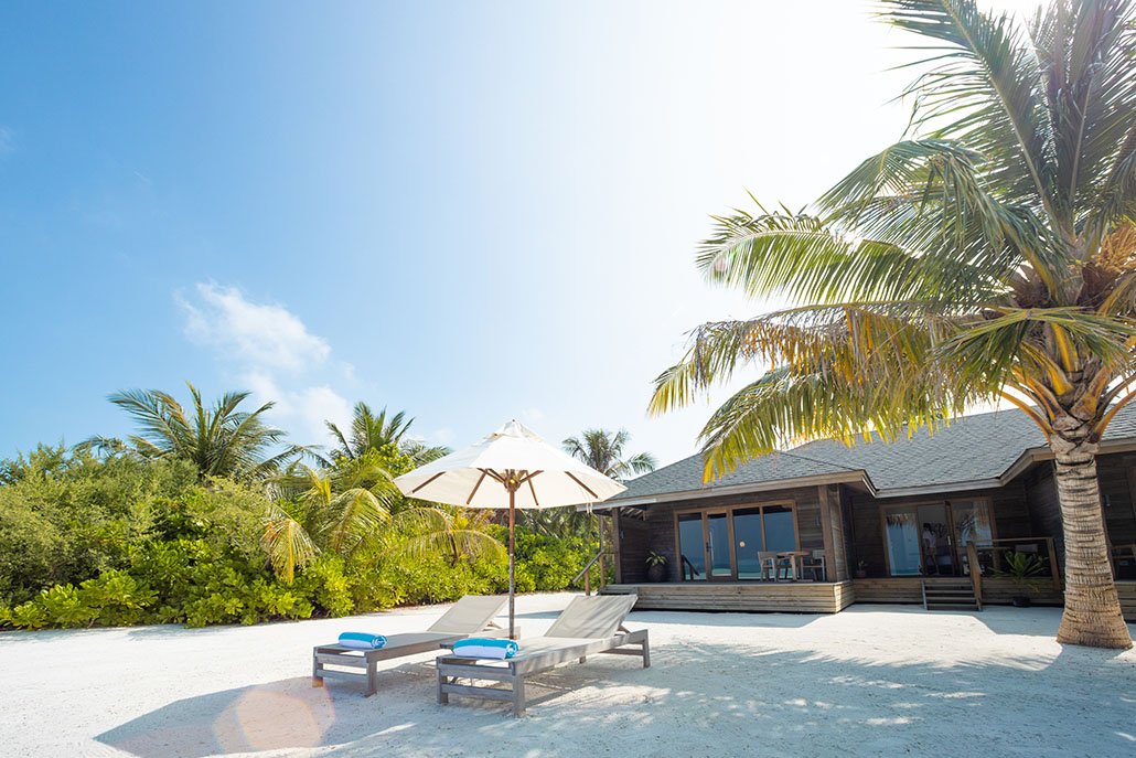 Jawakara Dheru Island beachfront villa with sun loungers under palm trees on white sandy beach