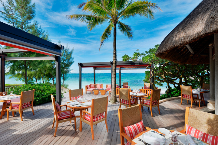 Oceanfront dining area at Constance Belle Mare Plage with tables under the shade of palm trees