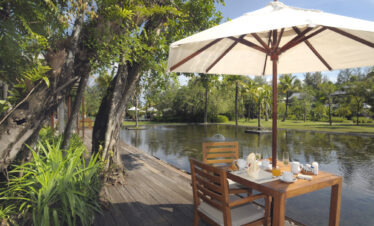 Outdoor breakfast table by a pond under an umbrella at The Sarojin Khao Lak surrounded by greenery
