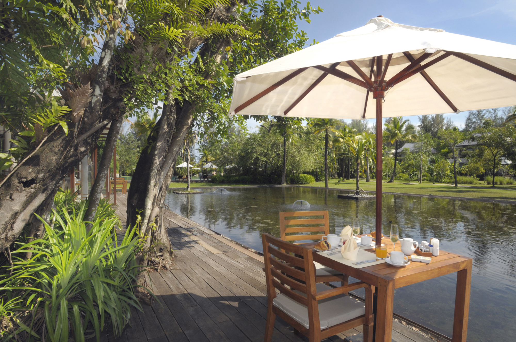 Outdoor breakfast table by a pond under an umbrella at The Sarojin Khao Lak surrounded by greenery
