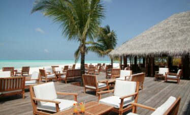 Outdoor deck with wooden furniture under palm trees at Meeru Island Resort offering stunning ocean views