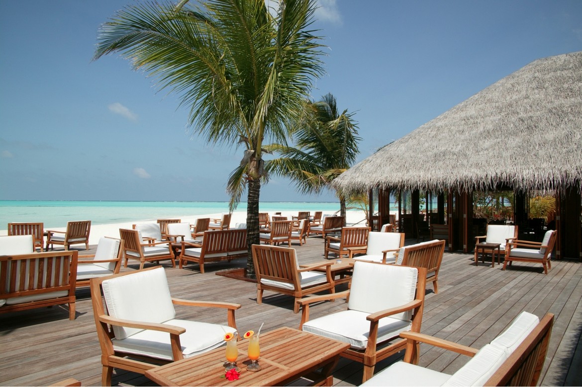 Outdoor deck with wooden furniture under palm trees at Meeru Island Resort offering stunning ocean views