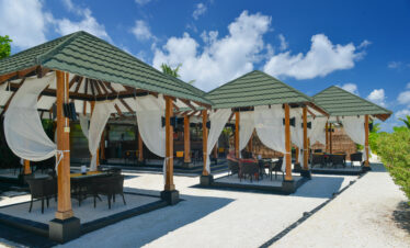 Outdoor dining area at Adaaran Meedhupparu with white curtains and roofed huts