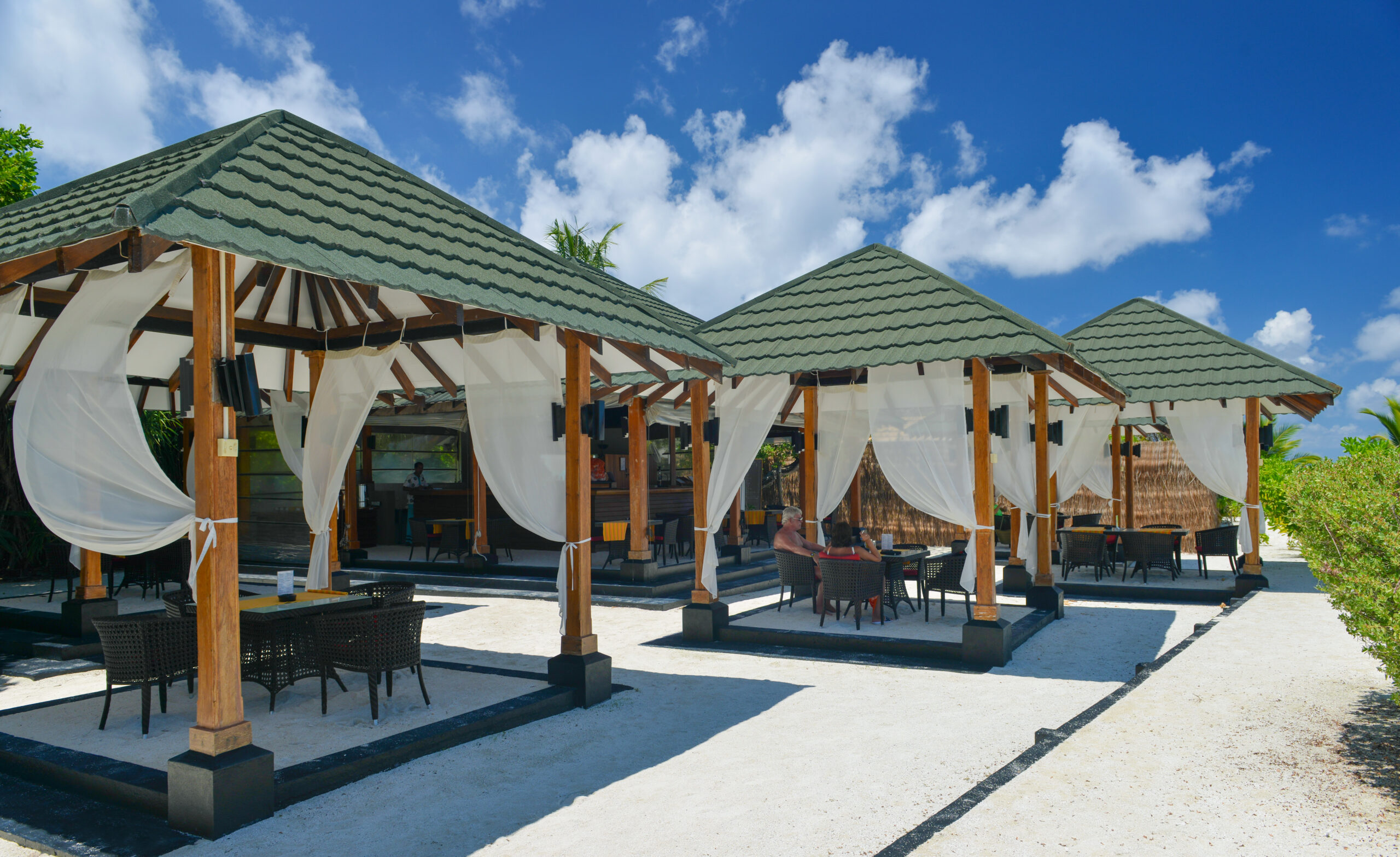 Outdoor dining area at Adaaran Meedhupparu with white curtains and roofed huts