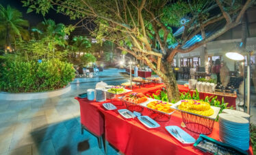 Outdoor dining setup at Chada Thai Village featuring buffet tables under a large tree surrounded by lush greenery
