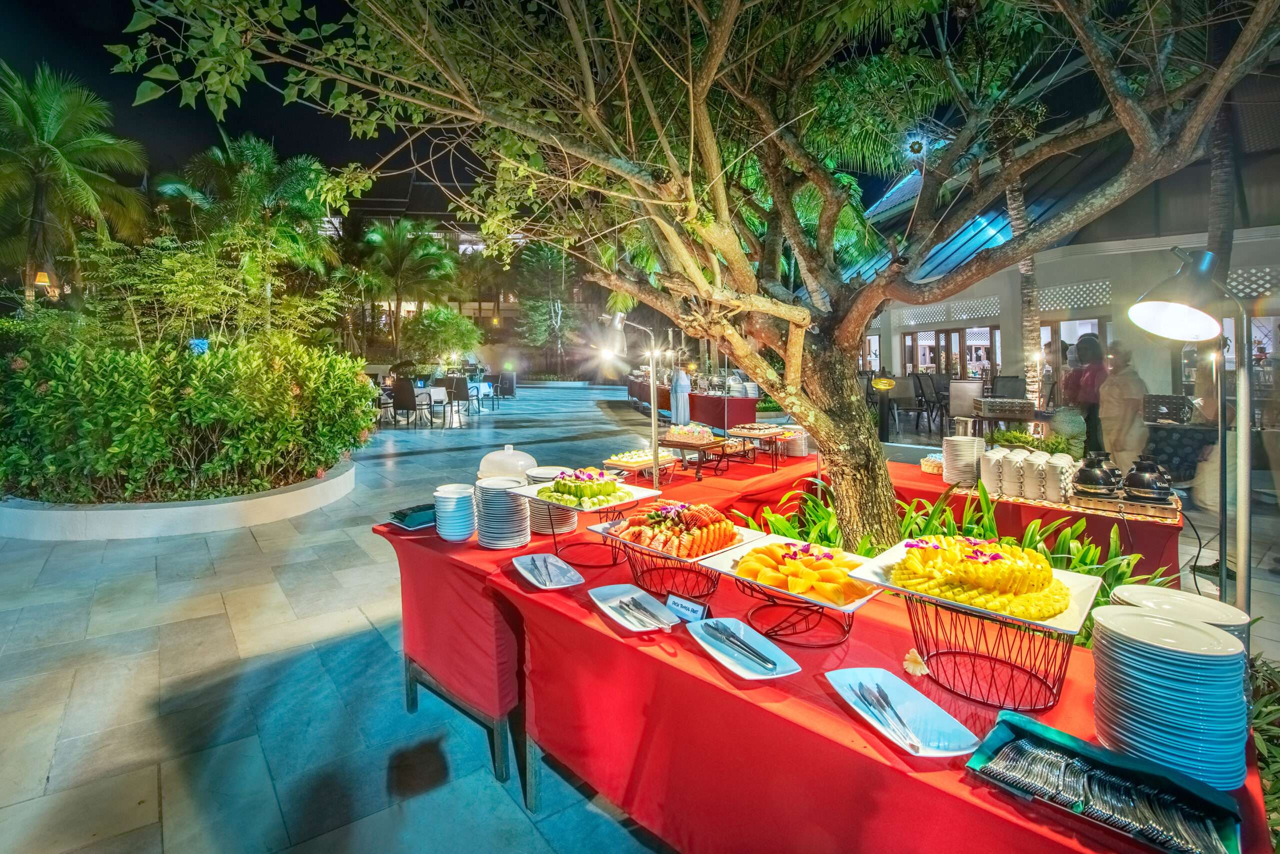 Outdoor dining setup at Chada Thai Village featuring buffet tables under a large tree surrounded by lush greenery