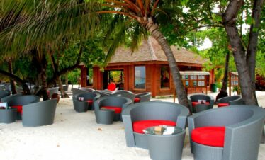 Outdoor lounge area at Meeru Island Resort with comfortable seating under palm trees on a sandy beach near the resort