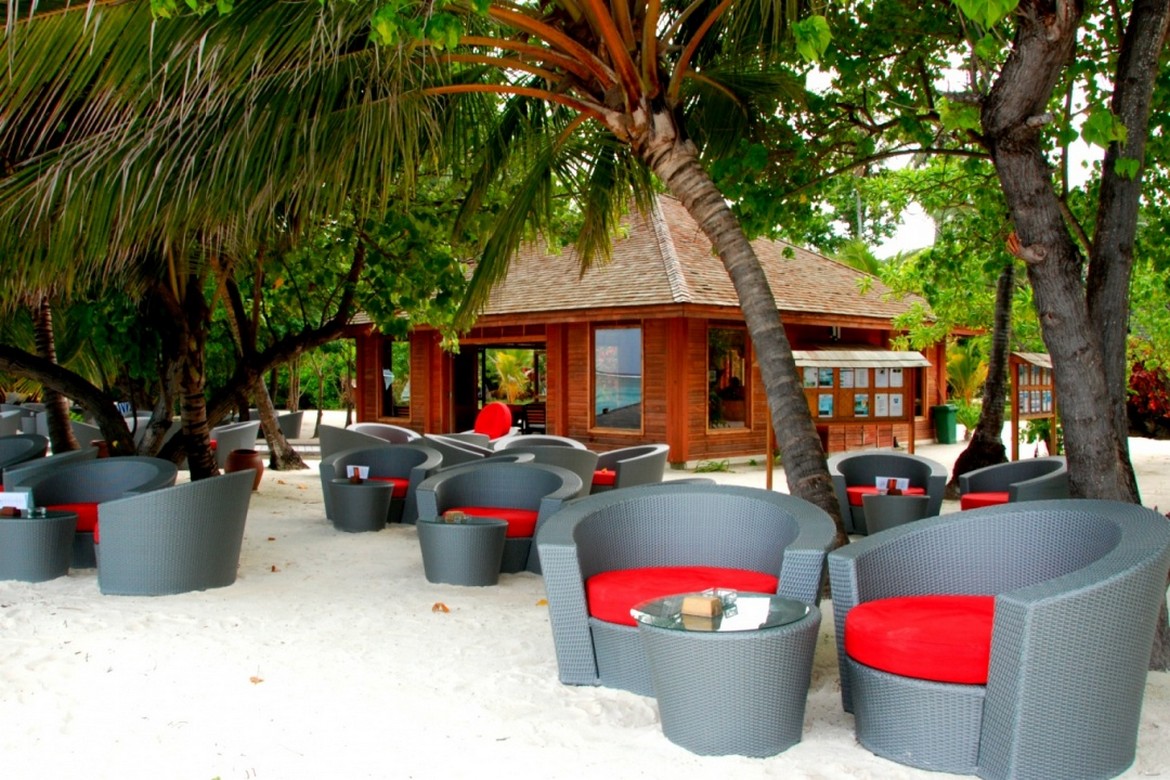 Outdoor lounge area at Meeru Island Resort with comfortable seating under palm trees on a sandy beach near the resort