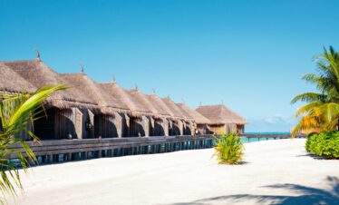 Overwater bungalows on a pristine beach at Constance Moofushi with thatched roofs and lush greenery