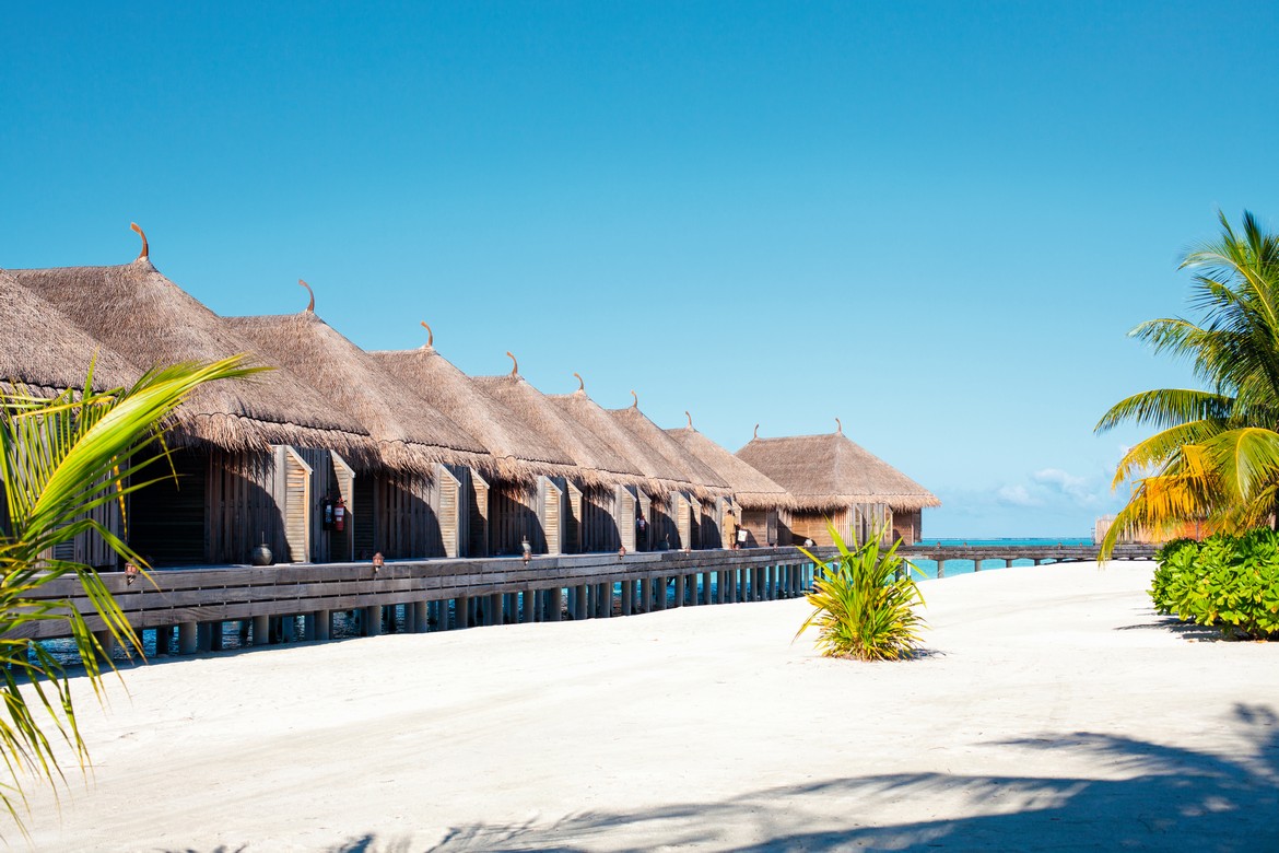 Overwater bungalows on a pristine beach at Constance Moofushi with thatched roofs and lush greenery