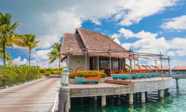 Overwater restaurant at Ayada Maldives with a thatched roof and ocean views on a sunny day